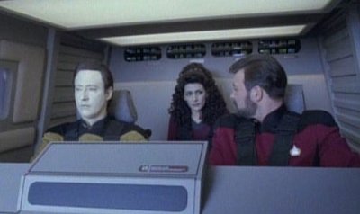 Riker and Data sit at the controls of the shuttlecraft with Riker turning to look at Deanna who sits behind them. All 3 have the seat belt harness on but they look to be manual not automatic ones